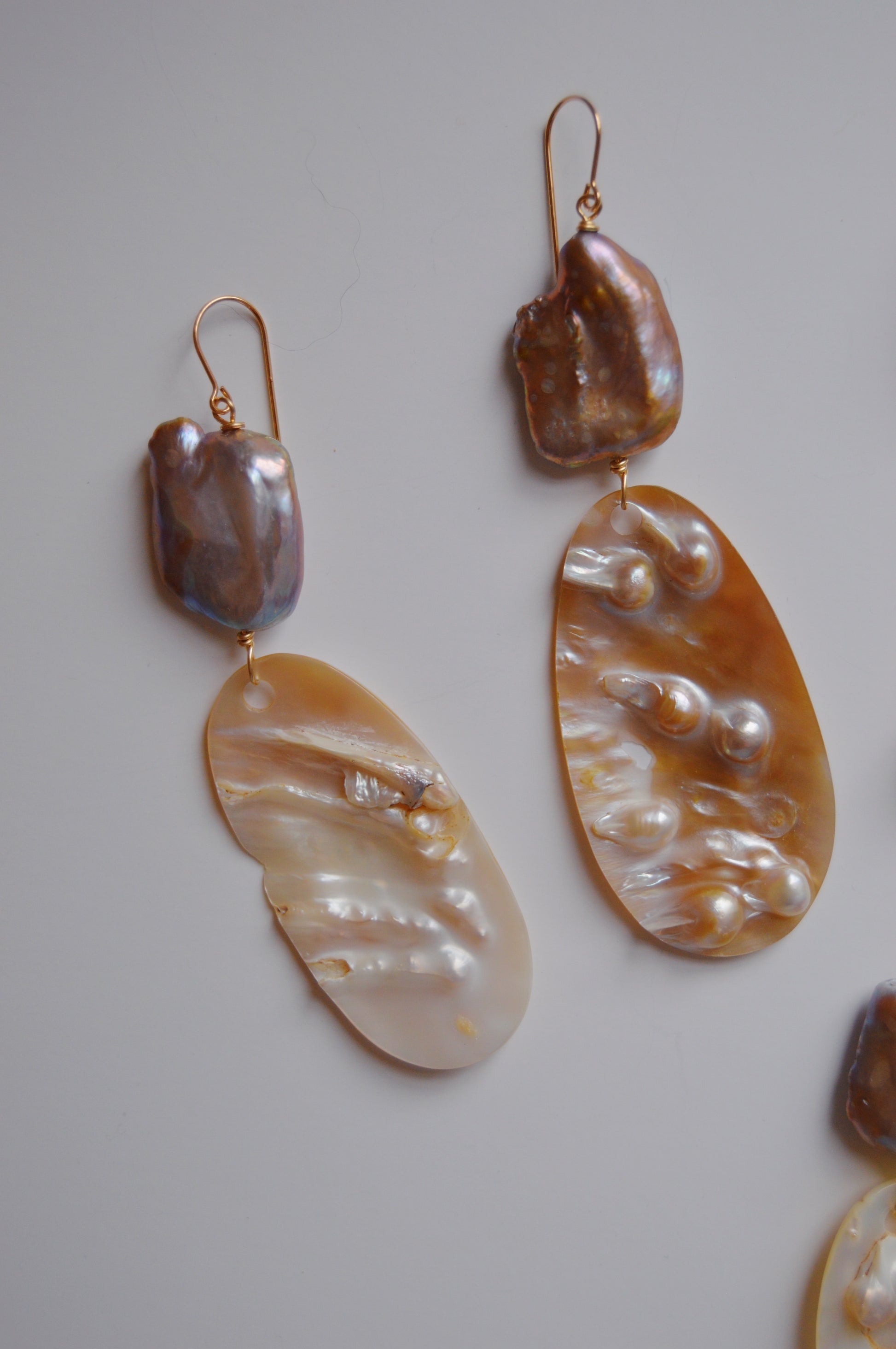 Angel Shell Drops: Mismatched handcrafted earrings with irregular iridescent stones atop elongated textured mother-of-pearl shell pieces, set against a plain, light background.