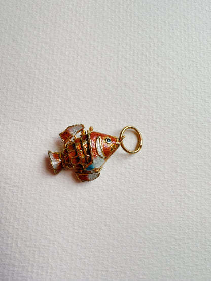 The Fish Anklet features a small, decorative cloisonné fish charm with orange, gold, and blue details and a gold ring—ideal as an accent for sterling silver anklets. Shown lying on a textured white surface.