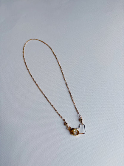 The Clasp in Front Layer necklace features a delicate 14K gold filled heart and small amber bead on a 16-inch chain, shown against a plain white background.