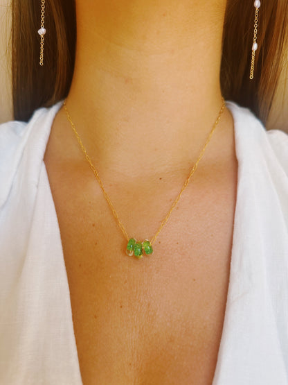 A close-up of a person wearing the Dainty Donut Layer— a 14K gold chain necklace with three green gemstone beads, paired with a white V-neck top and gold drop earrings. This elegant piece includes a secure gold filled clasp for added sophistication.
