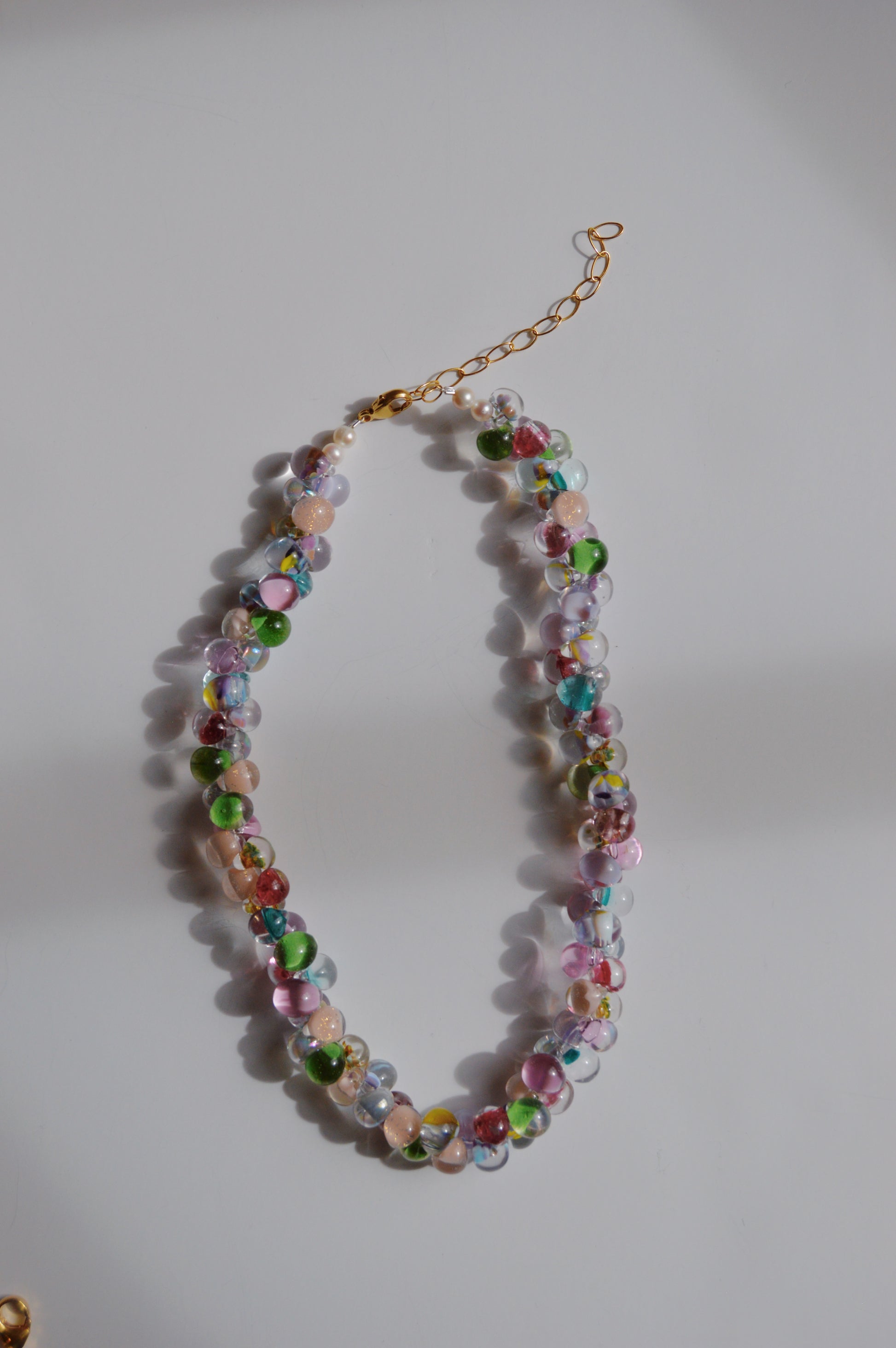 The Bubble Glass Necklace- Bloom Mix features colorful, round handmade glass beads in shades of green, pink, blue, and clear with a gold adjustable chain clasp.