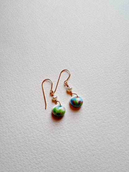 Bubble Minis are dangling earrings with gold hooks and gold-filled findings, each adorned with a freshwater pearl and a marbled blue, green, and pink round glass bead, shown against a white textured background.
