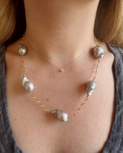 A close-up of a person wearing the Silver Organic Pearl Layer: a gold chain necklace with large organic silver pearls, paired with a delicate 14K gold filled chain and small round pendant, shown against a grey V-neck top.
