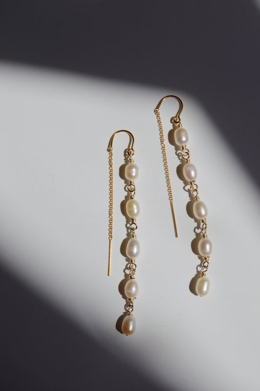 Pearl Threaders featuring delicate gold chains and several cultured freshwater pearls are displayed on a white surface, with dramatic shadows crossing part of the image.