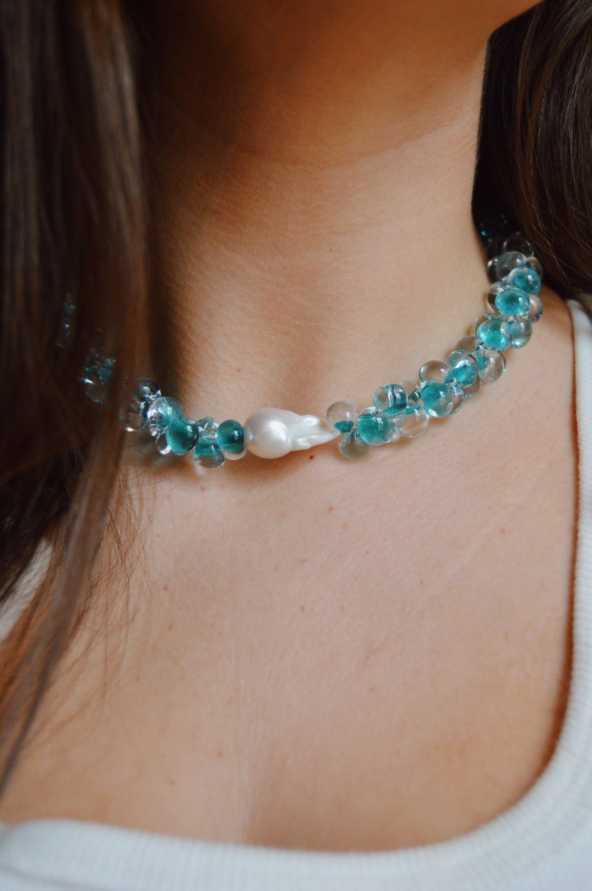Close-up of a woman's neck wearing the Bubble Glass Necklace- Bora Bora, featuring handmade glass beads, gold-filled findings, and a prominent central freshwater pearl against a neutral background.