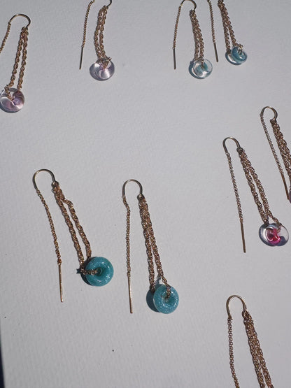 Glass Donut Threaders—14k gold filled chain earrings with small handblown glass beads in pink, blue, and clear—are displayed on a white textured surface, sunlight casting gentle shadows around them.