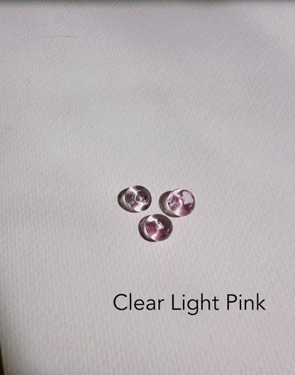 Three small, round, clear light pink Glass Donut Threaders rest on a white textured surface with “Clear Light Pink” below—perfect accents for handblown glass beads or delicate 14k gold filled chain jewelry.