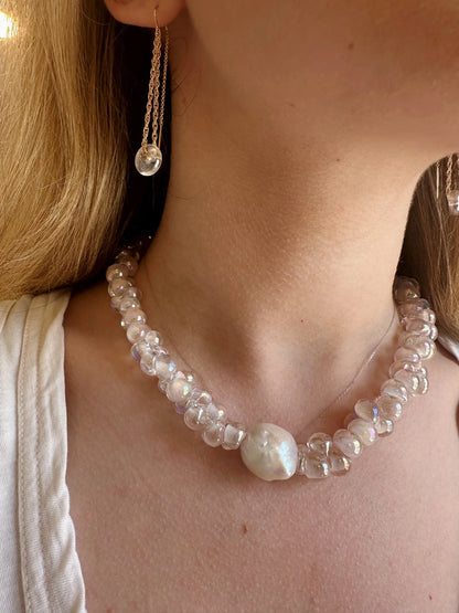 A close-up of a person wearing Glass Donut Threaders—14k gold-filled chain earrings with clear, iridescent handblown glass beads and a central large white pearl.