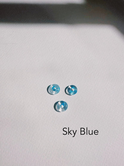 Three small, round, translucent blue Glass Donut Threaders resembling handblown beads are arranged in a triangle on a white textured surface. "Sky Blue" is printed in black text below the threaders.