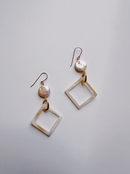 The Diamond Shell and Pearl Drops feature dangle earrings with cultured freshwater pearl studs and open diamond-shaped shell pendants, connected by gold-filled findings, shown on a simple light background.