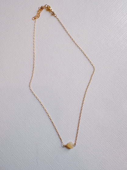 The Boyfriend Necklace, a delicate gold filled chain with a small light-colored stone pendant, is displayed on a white textured surface.