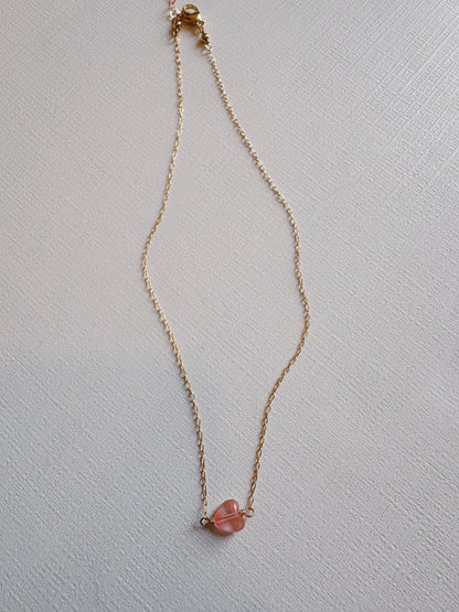 The Boyfriend Necklace—a delicate gold filled chain with a small pink gemstone pendant—is displayed on a textured white surface.