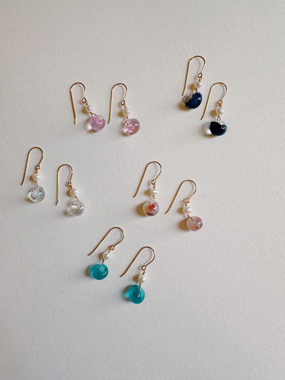 Nine pairs of Bubble Minis dangle earrings, each with gold filled findings, a freshwater pearl, and a colorful round glass bead, are arranged neatly on a plain white surface.