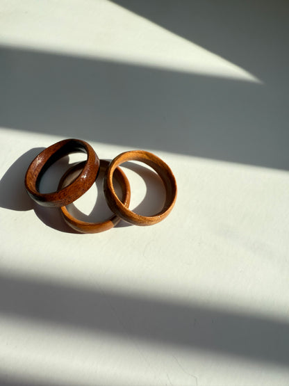 The Wooden Ring- Medium Wood rests on a white surface, bathed in bright sunlight that casts striking shadows and diagonal patterns across the scene.