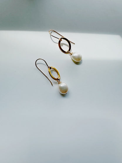 Gold Filled Pearl Drops earrings, featuring oval gold hoops with dangling cultured freshwater pearls, are displayed on a plain light gray surface in soft natural light.