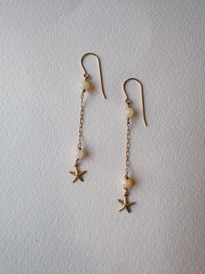 Starfish and Opal Drops: Elegant 14k gold filled dangle earrings featuring small pearls and star-shaped charms, shown on a textured white surface.