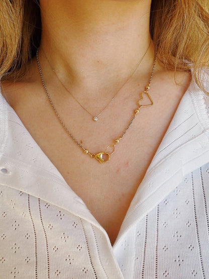 A woman in a white textured blouse wears the Clasp in Front Layer: a fine chain with a small round pendant and an oxidized sterling silver chain with a 14K gold-filled, heart-shaped outline adorned with circular details.