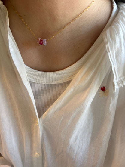 Close-up of a person wearing a white shirt and the Dainty Donut Layer—a 14K gold chain necklace featuring pink and purple glass donut beads—layered over a white top.