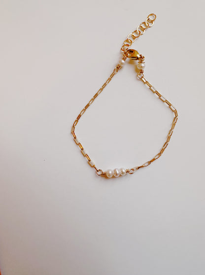 The Baby Bracelet is a delicate 14k gold filled chain with three small cultured freshwater pearls in the center, featuring a lobster clasp and adjustable links, displayed on a plain white background.