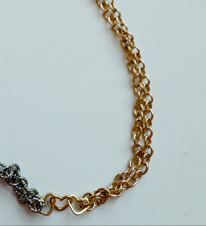 A close-up of the 2026 Winterfest Bracelet shows two intertwined chains on a white background: one is a 14k gold filled oval-link chain, the other a dark, textured oxidized sterling silver chain.
