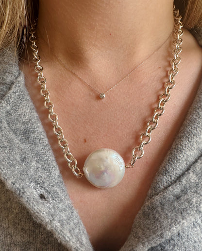 Close-up of a person wearing the Sterling Chunky Pearl Layer necklace—a bold sterling silver chain with a large cultured freshwater pearl pendant—paired with a delicate single gem necklace, styled over a gray textured top.
