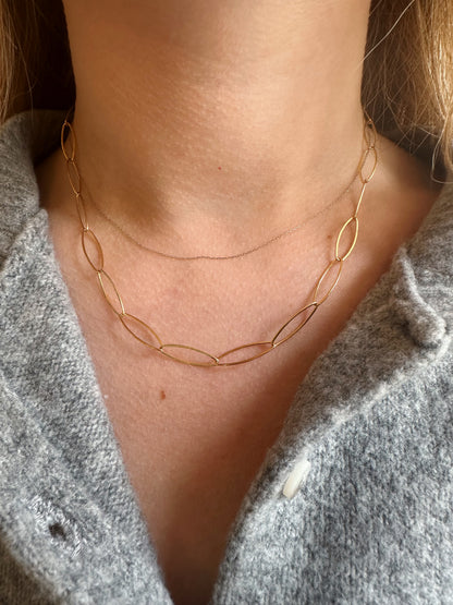 A close-up of a person's neck wearing the Gold Filled Almond Layer, a delicate 14k gold filled chain with oval links, paired with a soft grey buttoned-up top.