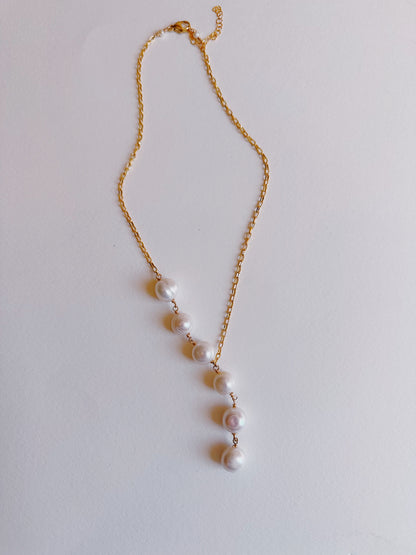 The 6 Pearl Lariat - White Pearls features a 14k gold filled chain with six cultured freshwater pearls arranged vertically and evenly spaced along the lower part of the chain, displayed on a plain white background.