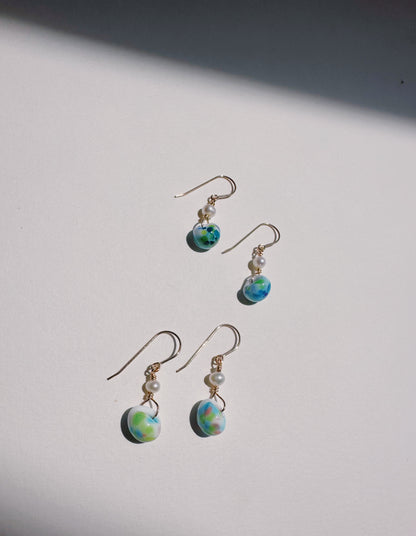Four Bubble Minis earrings with gold-filled findings, each featuring a freshwater pearl and a green-blue marbled glass bead, are displayed on a white surface in soft natural light and shadow.