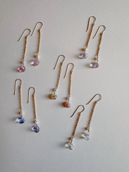 Eight pairs of Bubble Drops gold chain earrings with handblown glass beads in pastel shades—pink, purple, blue, orange, and clear—are arranged neatly on a light background.