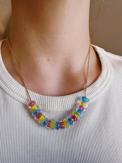 A person wears the Lots of Donuts Layer: a 14k gold filled chain necklace featuring handblown glass beads in blue, yellow, and pink, paired with a white ribbed shirt.