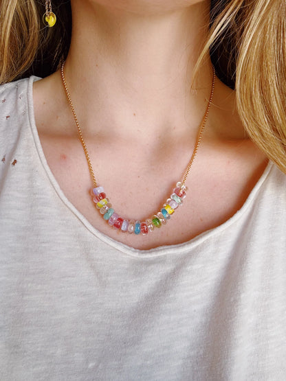 A close-up of a person wearing a cream shirt and the Lots of Donuts Layer—a 14k gold filled chain necklace featuring a row of colorful, handblown glass beads across the collarbone.