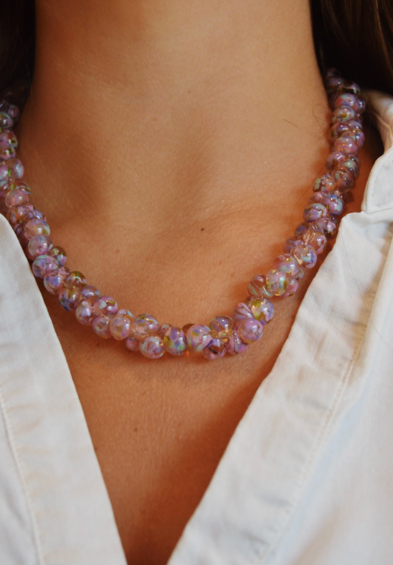 A close-up of a person wearing a white collared shirt and the Print Bubble Glass Necklace, featuring round, translucent purple glass beads with hints of iridescent colors.