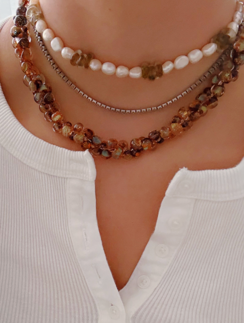 A person in a white button-up shirt wears the Print Bubble Glass Necklace layered with a freshwater pearl strand and a thin 14k gold-filled chain. The photo is cropped to feature only the neck and collar area.