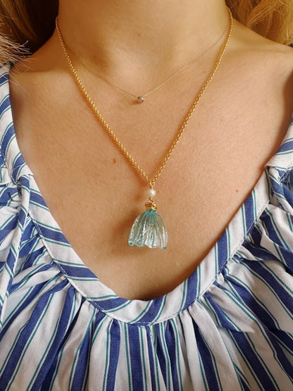 A person in a blue and white striped top wears two necklaces: the Tulip Necklace—a 14k gold filled chain with a clear handblown glass tulip pendant—and a shorter, delicate chain with a small round charm.