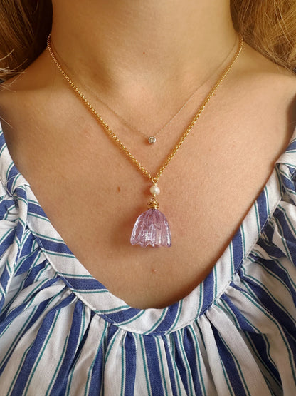 A person in a blue-and-white striped top wears two gold necklaces: one with a tiny round diamond pendant, and the Tulip Necklace, which showcases cultured freshwater pearls and a striking lavender crystal pendant.