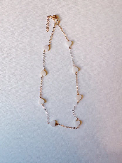 The Mixed Metal Mother of Pearl Layer features a delicate gold filled chain with evenly spaced heart-shaped mother of pearl beads, elegantly displayed on a textured white background.