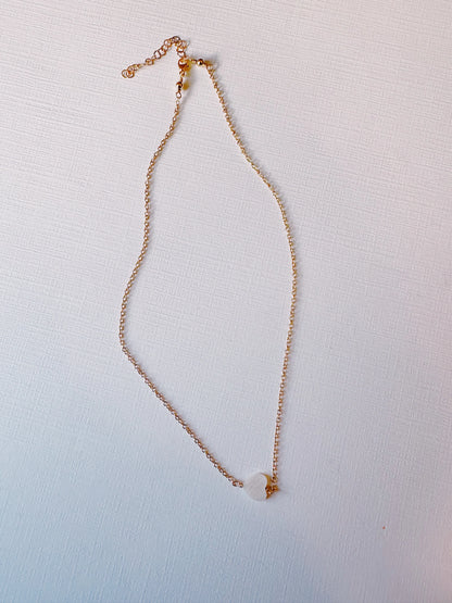 The Dainty Mother of Pearl Layer features a 14k gold filled chain necklace with a single mother of pearl heart pendant, elegantly displayed on a textured white surface.