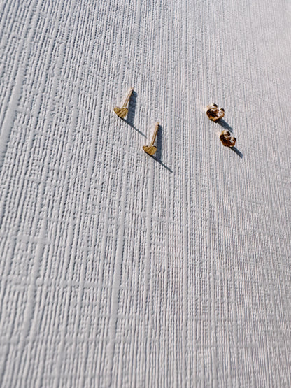 The Mini Heart Studs, two small 14k gold filled heart earrings with butterfly backings, are displayed on a textured white surface featuring vertical and horizontal lines.