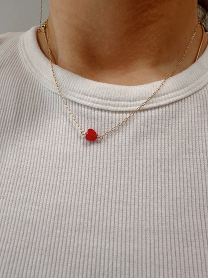 A person wearing The Boyfriend Necklace, a thin gold filled chain with a small red heart gemstone pendant, paired with a ribbed white shirt.