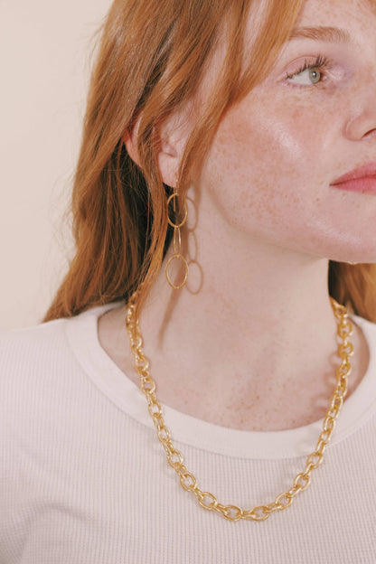 A woman with long red hair and freckles wears a white top, gold hoop earrings, and the Chunky Plated Layer necklace.