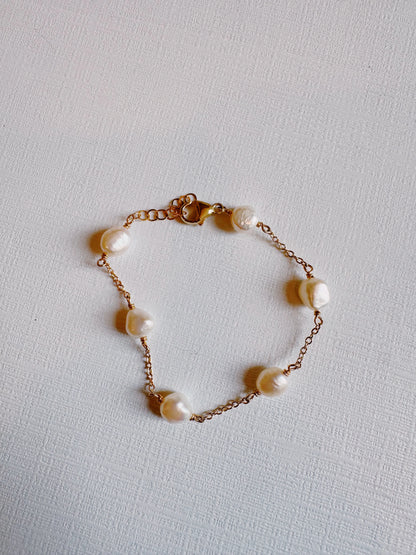 The Pearl Bracelet features a hand-wired 14k gold filled chain with seven irregularly shaped white cultured freshwater pearls, spaced evenly and shown on a textured white surface.