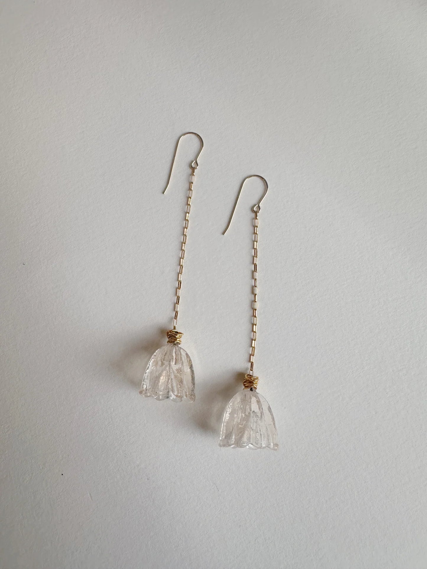 Glass Tulip Earrings in blush feature long 14k gold-filled chains and hooks, each adorned with a handcrafted clear, flower-shaped glass pendant, shown on a white background.