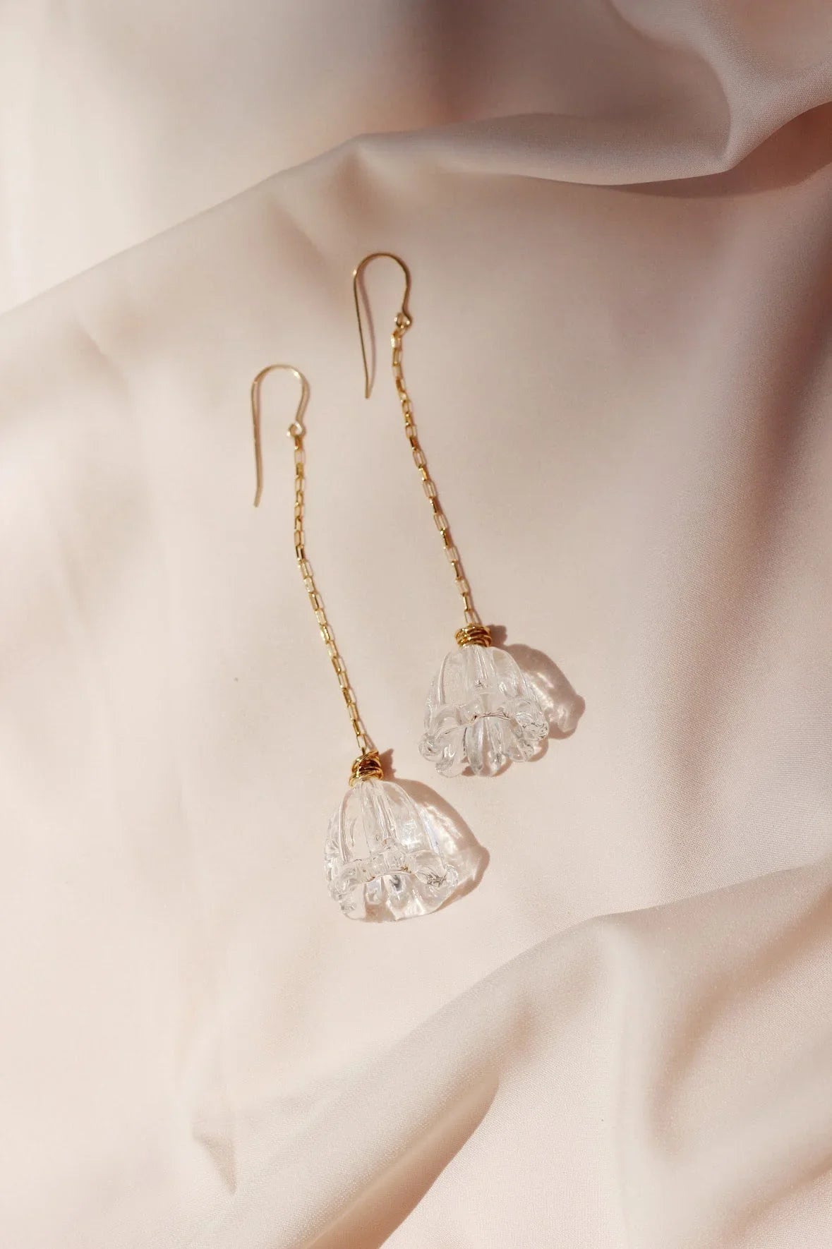 Glass Tulip Earrings: Clear, flower-shaped glass pendants handmade by a glass artist hang from 14k gold-filled chains for an elegant touch. Displayed on soft light beige satin fabric.