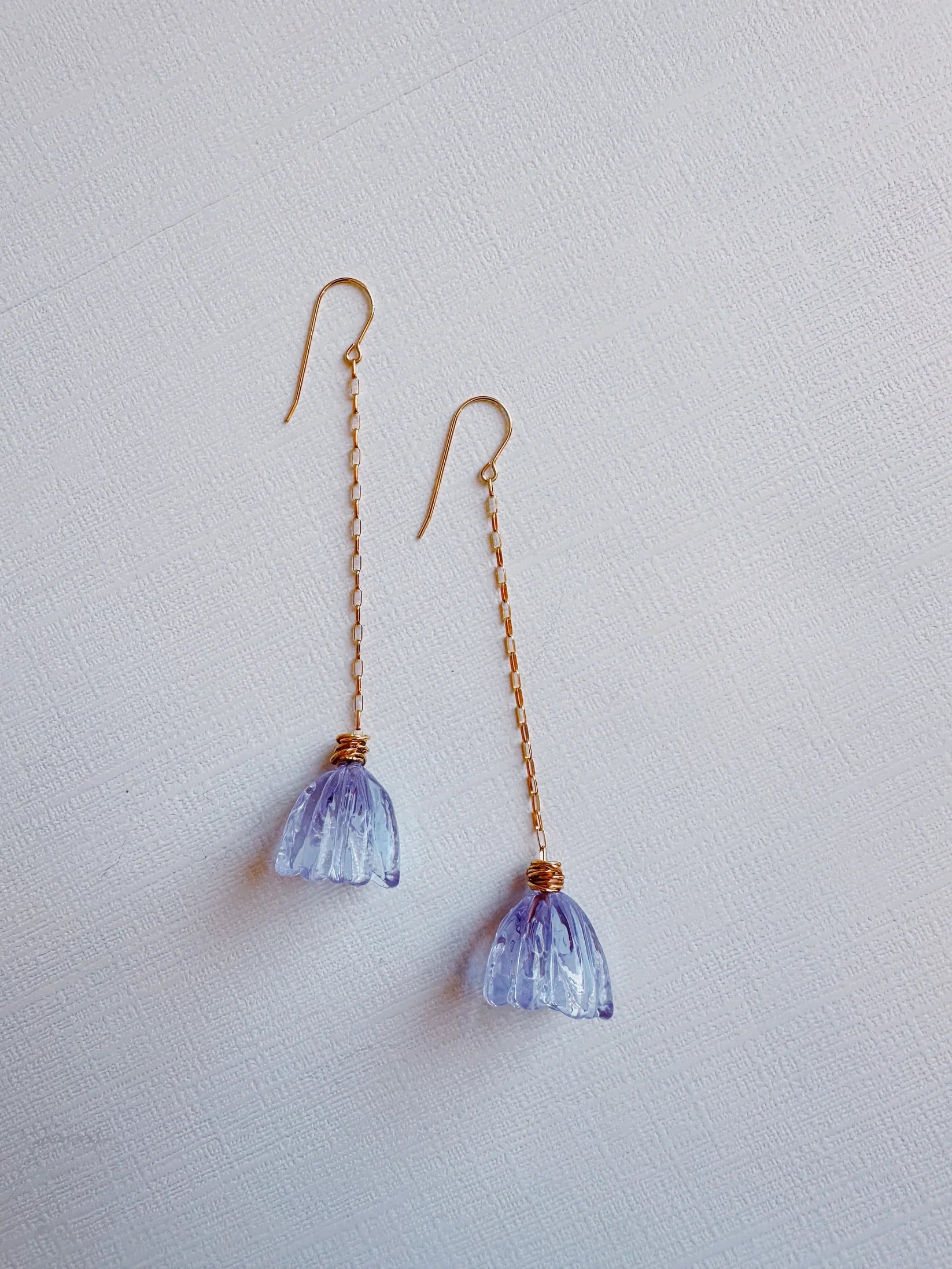 Glass Tulip Earrings in lavender feature delicate handmade lampwork tulip charms on 14k gold-filled threader chains, displayed on a white textured surface for an elegant look.