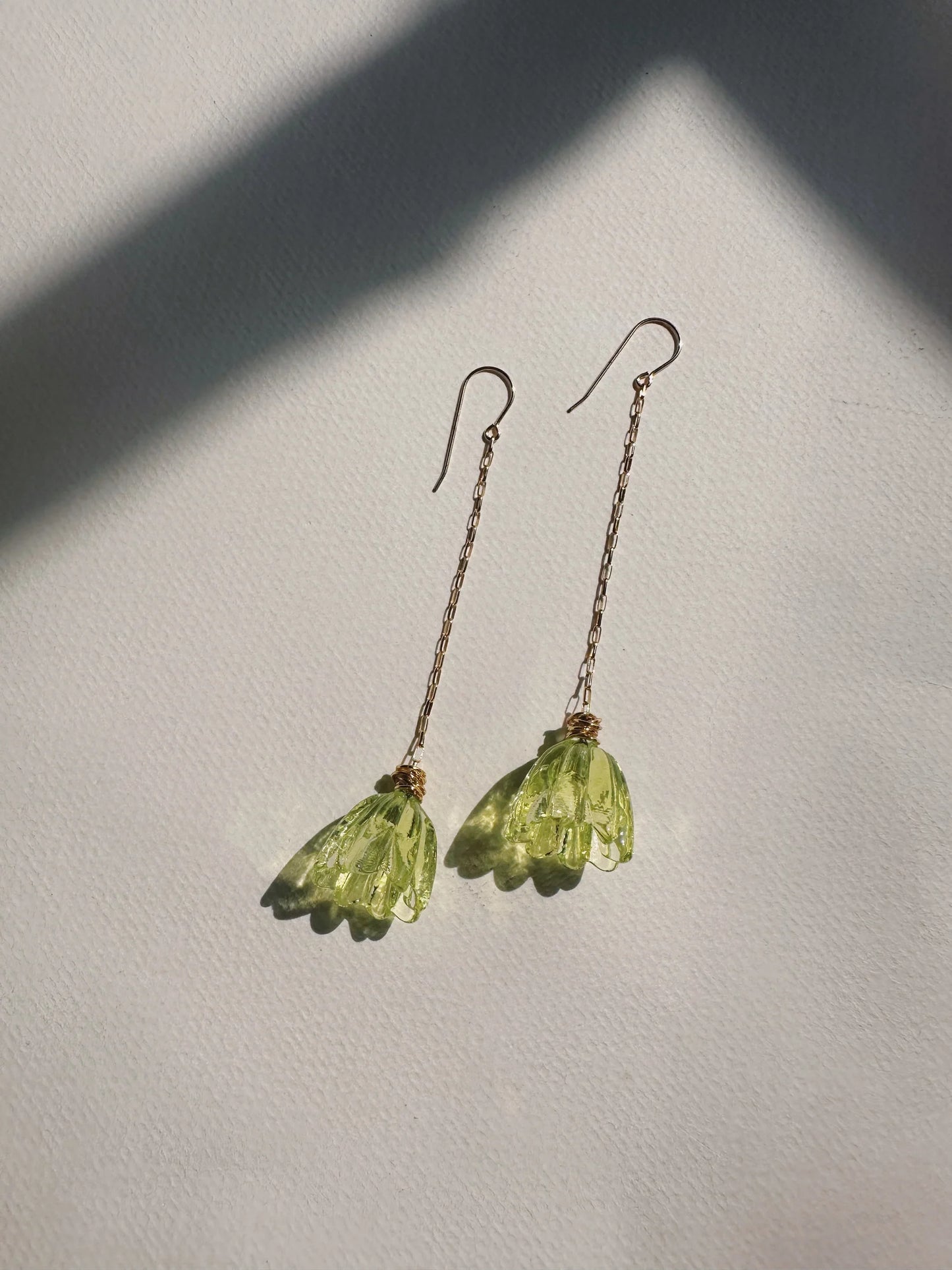 Glass Tulip Earrings in light lime feature delicate 14k gold-filled chains with handmade translucent green lampwork tulips, shown on a white textured surface with gentle sunlight and soft shadows.
