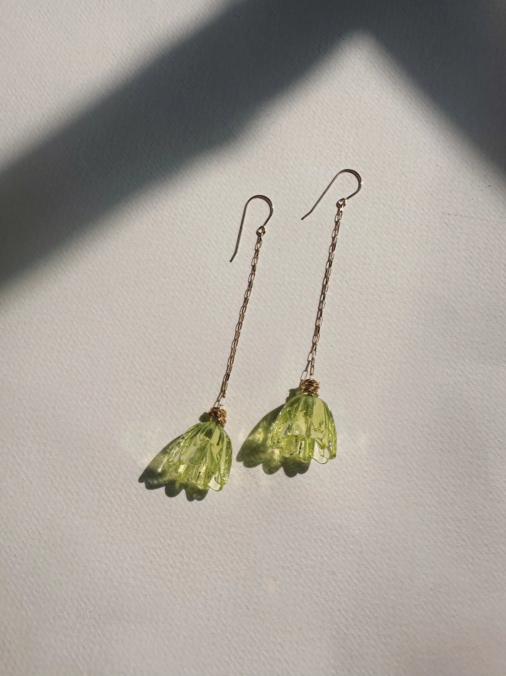 Glass Tulip Earrings in light lime feature delicate 14k gold-filled chains with handmade translucent green lampwork tulips, shown on a white textured surface with gentle sunlight and soft shadows.