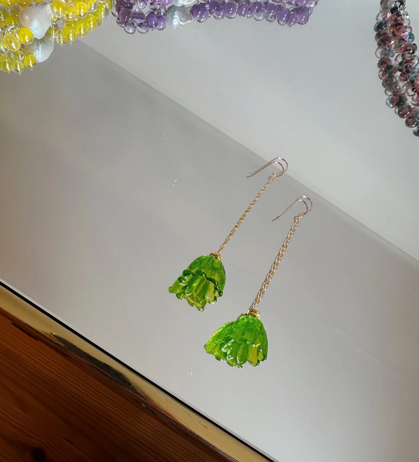 Glass Tulip Earrings in lime feature long 14k gold-filled chains and handmade glass tulip pendants, presented on a white surface with colorful artisan beaded jewelry in yellow, purple, and pink.