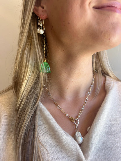 A woman with long blonde hair wears artisan jewelry: a pearl drop earring, handmade Glass Tulip Earrings in sea green, and a gold chain necklace with a large baroque pearl pendant. She is dressed in a light-colored top.
